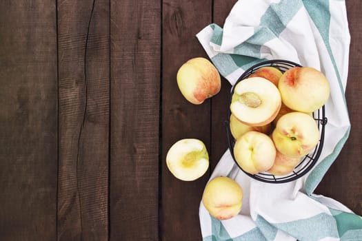 Flat lay with large and big juicy organic peaches in the metal basket near kitchen towel on brown wooden table background with old boards. Natural fruits, copy space. Full and halved cuts of peach