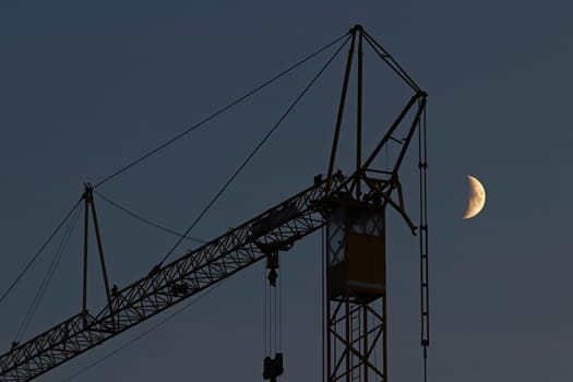Moonlighting in the construction industry. A crane and the moon in the night sky