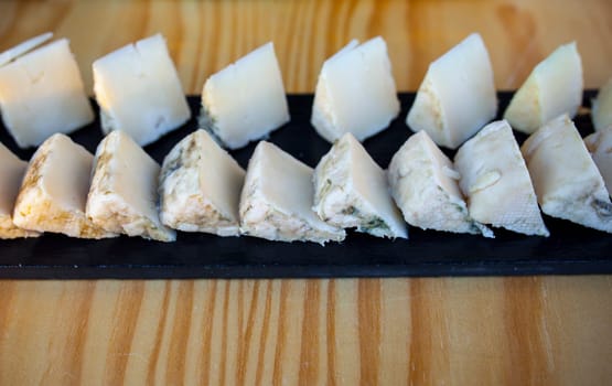 Slices of tender rosemary goat cheese over black slate tray. Closeup