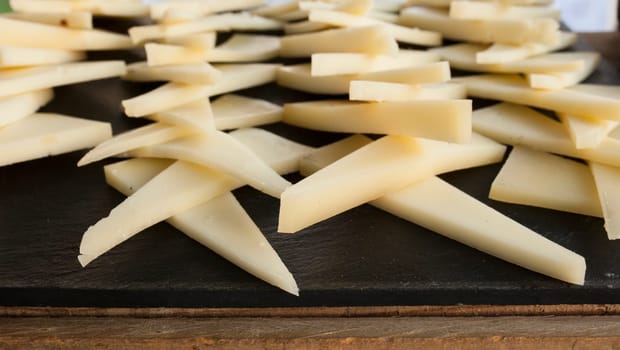 Cured slices of manchego cheese over black slate tray. Closeup