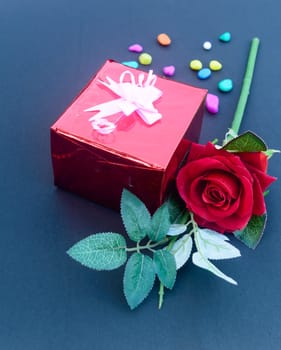 A red rose and a wrapped gift box with ribbon on table in blue background. High angle view. Flat Lay. Copy space room for text.