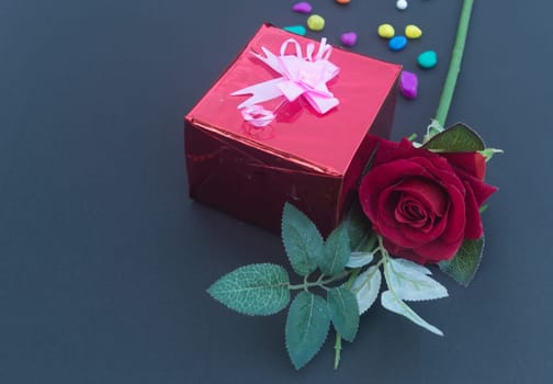 A red rose and a wrapped gift box with ribbon on table in blue background. High angle view. Flat Lay. Copy space room for text.