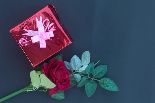 A red rose and a wrapped gift box with ribbon on table in blue background. High angle view. Flat Lay. Copy space room for text.