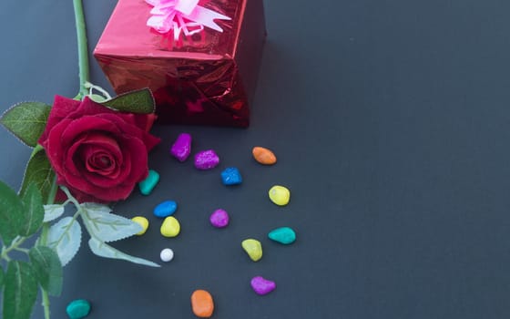 A red rose and a wrapped gift box with ribbon on table in blue background. High angle view. Flat Lay. Copy space room for text.