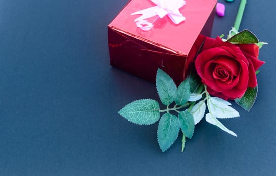 A red rose and a wrapped gift box with ribbon on table in blue background. High angle view. Flat Lay. Copy space room for text.