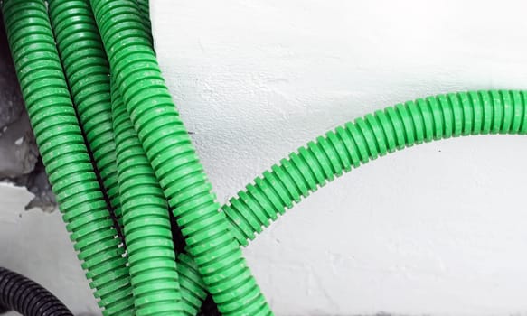 Corrugated tubular conduits ready to be filled with electrical cables on a construction site. White wall in the background. Construction material for securing electrical cables