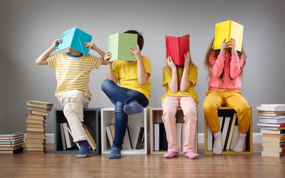 Group of children sitting on the book's stacks and on the bookshelves in the room and reading periodical. Concept of education and friendship.
