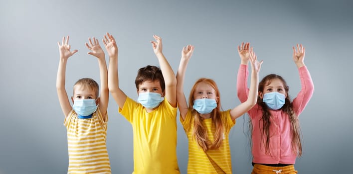 Group of four children in medical mask standing indoors with holding hands up. Concept fight with pandemic of Covid-19 and human relationship.