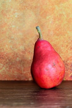 Still life of a rustic red pear against an orange background.