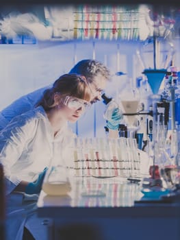 Scientists researching in scientific laboratory. Young female scientist and her senior male supervisor looking at the cell colony grown in the petri dish in the life science research laboratory.