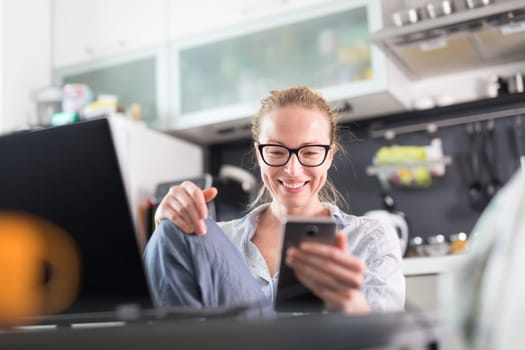 Stay at home and social distancing. Woman in her casual home clothing working remotly from kitchen dining table. Video chatting using social media with friend, family, business clients or partners.