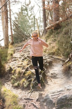 Active sporty woman running in autumn fall forest jumping over the roots on the path. Healthy lifestyle image of young active caucasian woman jogging outside in nature.