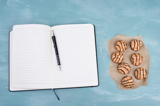 Coconut macaroons on a textured blue background, empty booklet with a pen