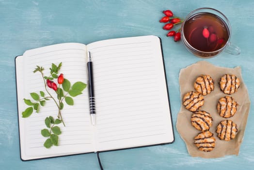 Coconut macaroons on a textured blue background, empty booklet with a pen, cup of tea