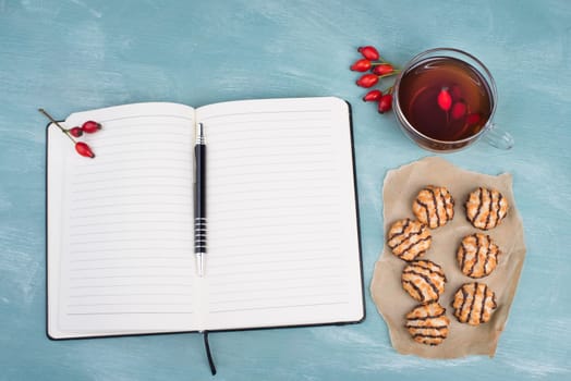 Coconut macaroons on a textured blue background, empty booklet with a pen, cup of tea