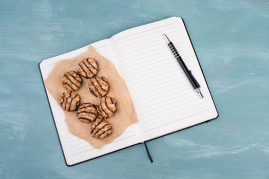 Coconut macaroons on a textured blue background, empty booklet with a pen