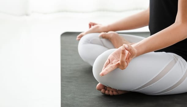 Woman practicing yoga in Lotus position or Padmasana with mudra. Cross-legged sitting meditation pose in white bedroom after wake up in the morning. Concept of exercise, relaxation and healthcare.
