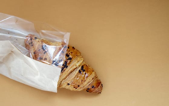 One regular fresh crispy whole grain croissant with chocolate filling on a brown or coffee background with copy space. Classic traditional freshly baked French dessert, pastries. Top view, flat lay