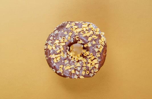 Fresh chocolate donut isolated on coffee background. Delicious dessert with glossy chocolate glaze. Sweet food concept with one round chocolate donut for your design and print. Top view, flat lay
