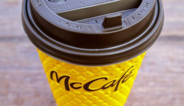 Paper yellow glass glass with coffee for McCafe drinks on the table against blurred city from McDonald's. Fast food business background. Fast food restaurant menu. Ukraine, Kiev - September 13, 2021