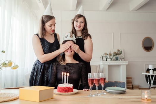 Two girls prepared a packed gift box for their birthday friend, closing eyes with hands, celebrating women's day, having glasses with champagne