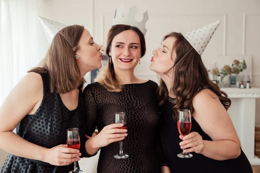 Womens party. Girlfriends girls in black dresses kiss the birthday girl. Glasses with pink champagne in hands. Hen-party