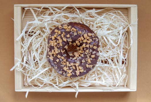 Fresh chocolate donut isolated on coffee background. Delicious dessert with glossy chocolate glaze. Sweet food concept with one round chocolate donut for your design and print. Top view, flat lay