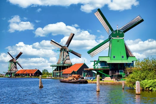 ZAANSE SCHANS, NETHERLANDS - CIRCA AUGUST 2020: Dutch windmill in green countryside close to Amsterdam, with blue sky and river water.