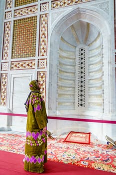 A woman dressed in a traditional omani abaya looking at an ornate alcove at the Muhammad al-Amin Mosque in Muscat, Oman