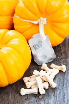 Halloween concept with miniature pumpkins, tombstone and bones candy on wooden table