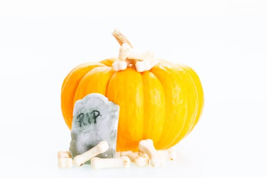 Halloween concept with miniature pumpkin, tombstone and bones candy over white background