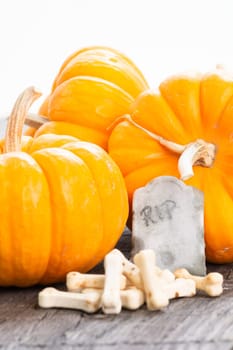 Halloween concept with miniature pumpkins, tombstone and bones candy on wooden table
