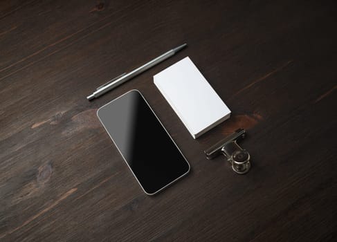 Smartphone and blank stationery: business card, pen and paper clip on wood table background. Template for branding identity.