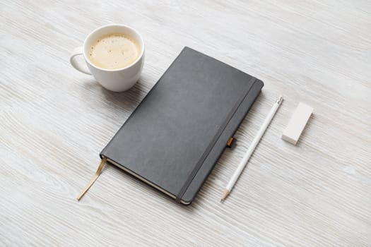 Photo of blank closed notepad, pencil, eraser and coffee cup on light wooden background. Responsive design mockup. Stationery elements. Template for placing your design.
