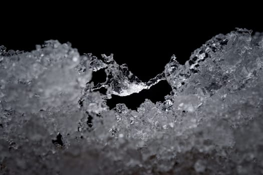 Super close up abstract image of slowly thawing snow. Minute detail of the ice crystals are visible, plain black background. Cold outdoor weather