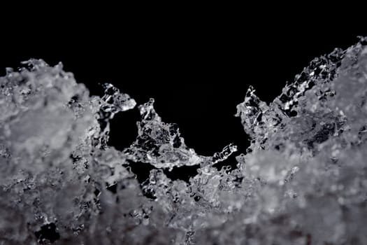 Intricate details of melting water particles. Focus on odd shaped ice crystal in the middle, but plain black background with copy space above.