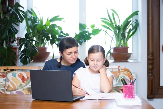 Distance learning concept. Mother helps her daughter to do school homework, using digital tablet, e-learning concept, home education.