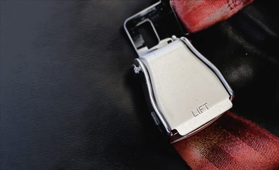 Red lap belt of an empty seat inside an airplane with the word LIFT embossed on the metal. Safe travel