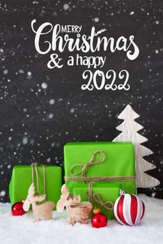 English Calligraphy Merry Christmas And A Happy 2022. Green Christmas Present With Red Decoration And Snow, Tree And Reindeer, Snowflakes