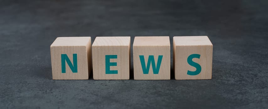 The word news is standing on wooden blocks, dark background