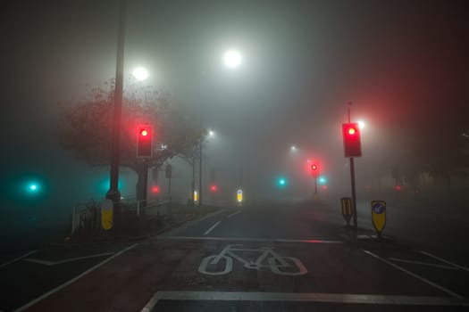 Colored traffic lights and white street lights shine through thick night time fog at a road junction near the hallamshire hospital in sheffield.
