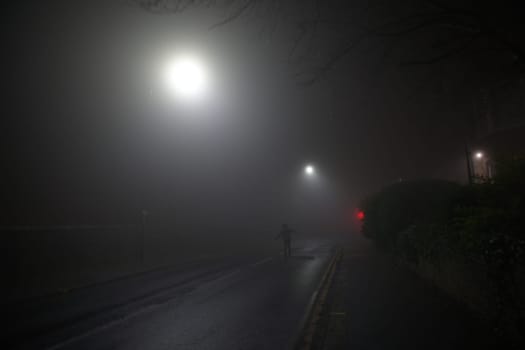Happy lone man enjoys freedom as he runs up a deserted street with arms outstretched. Extremely foggy weather conditions and night time street lights.