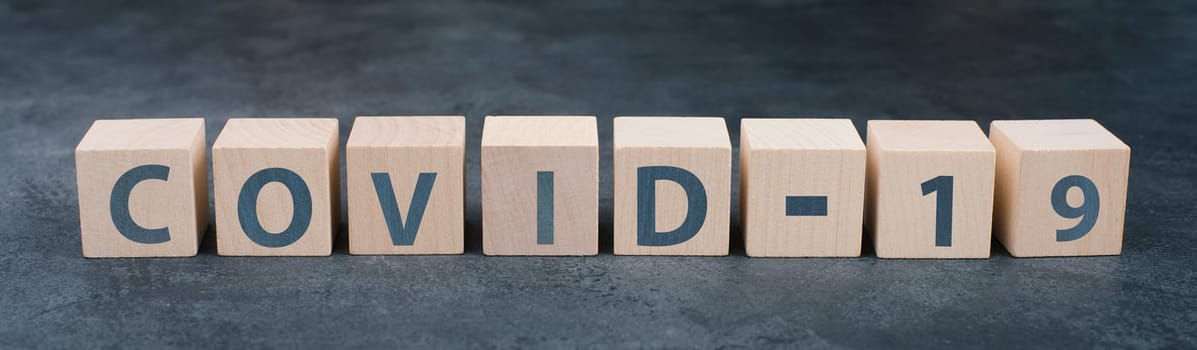 The word covid-19 is standing on wooden blocks, dark background, headline