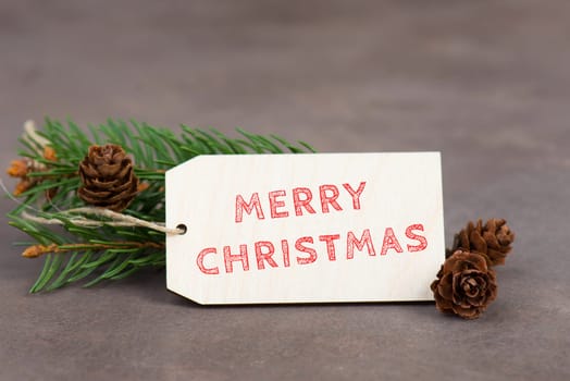 Merry christmas is standing on a sign, branch of fir and cones, textured brown background