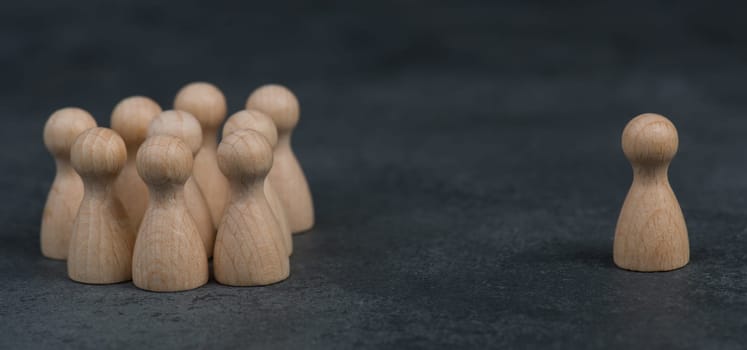 Group of wooden figures standing together, one leader standing alone on the opposite side