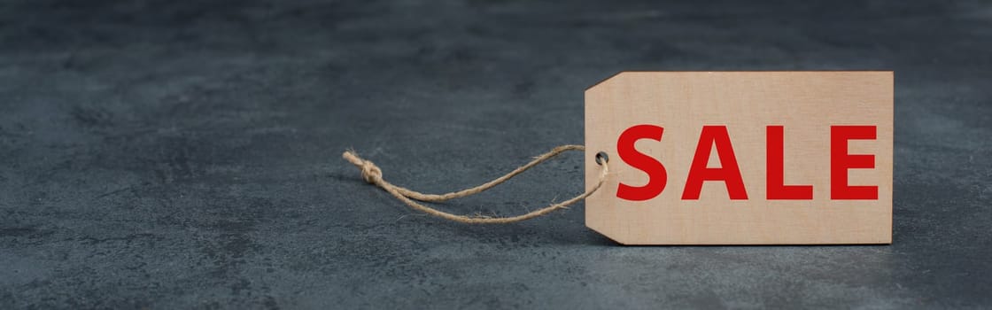 Wooden label with the word sale in red color, dark textured background, empty copy space