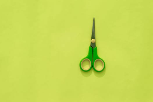 Green scissors isolated on Light green background. Table top view. Copy space for text.