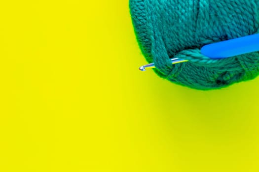 A metal hook with a blue handle is inserted into a skein of green yarn in the upper corner of the photo on a yellow background. top view, flat lay, copy space, isolate. High quality photo