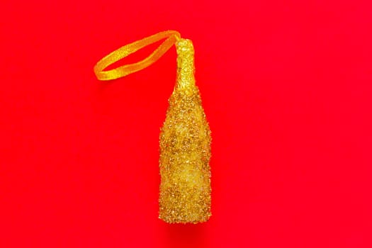 A toy for the Christmas tree in the form of a golden champagne bottle with sequins lies in the center on a red background. top view, flat lay, copy space, isolate. High quality photo