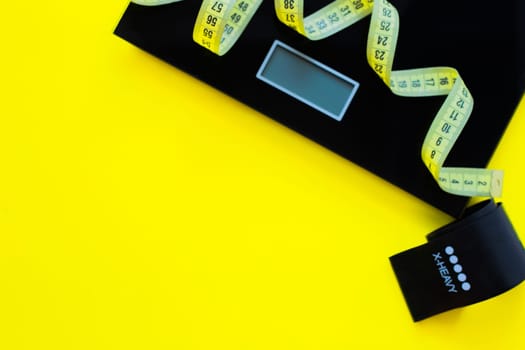 A weight scale, a black fitness tape and a yellow measuring tape lie on a yellow background on the side of the photo. top view, flat lay, copy space, isolate. High quality photo